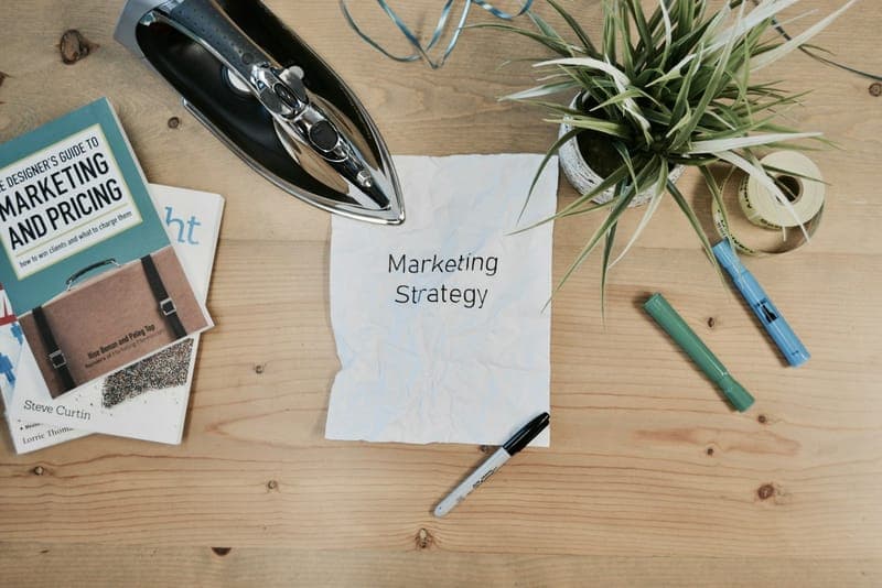 A desk with a marketing strategy notebook, stationery and a plant.
